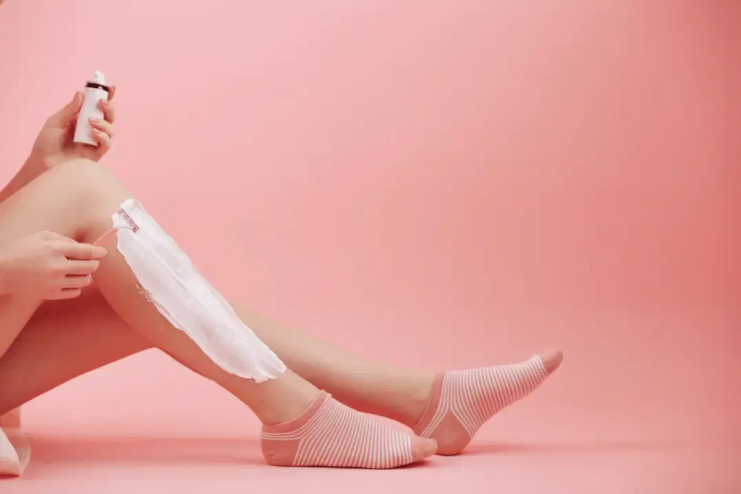 Body razor designed for intimate shaving, sitting on a towel beside sensitive-skin shaving cream