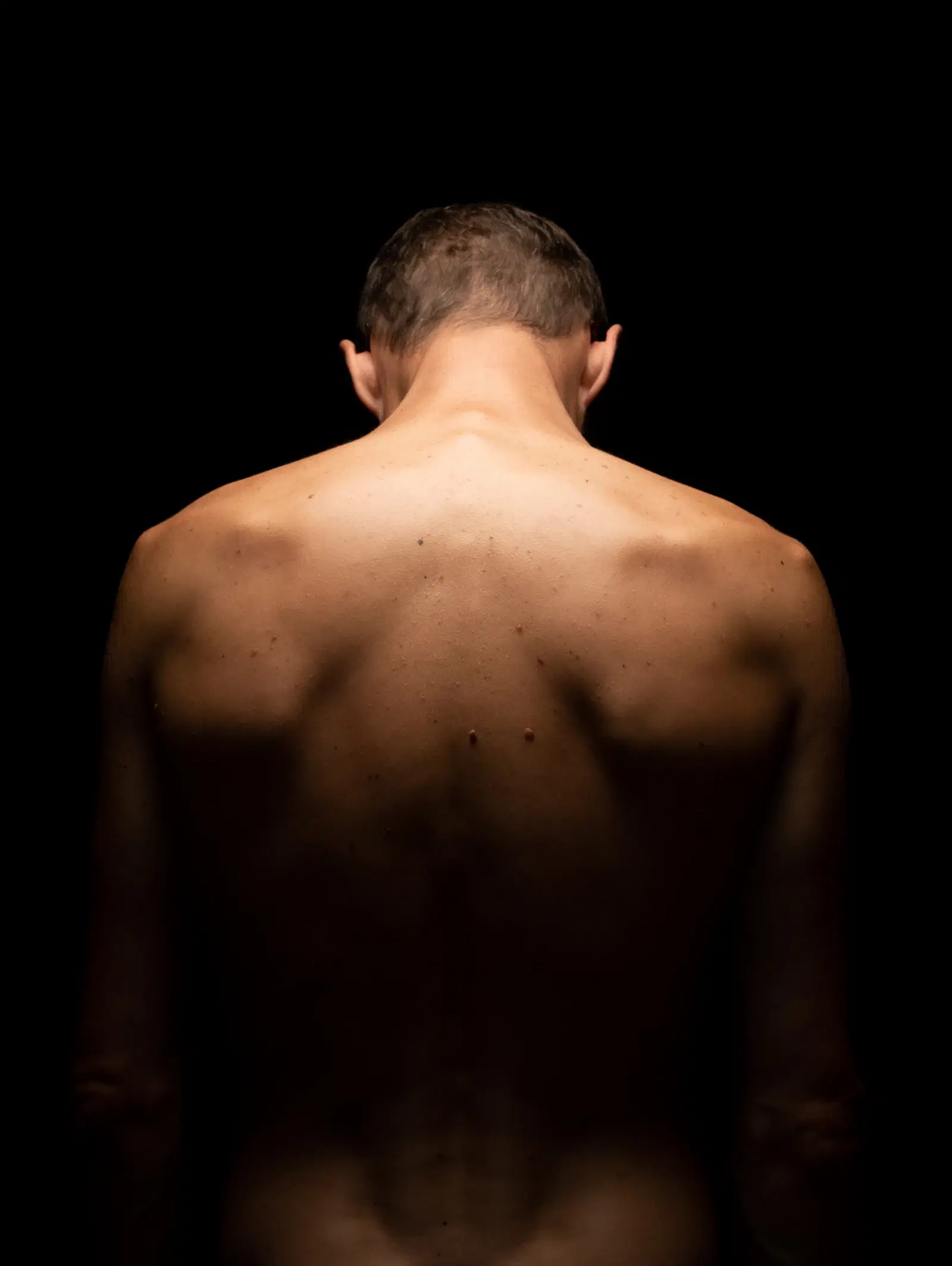 A man's bare back and shoulders lit against a dark background