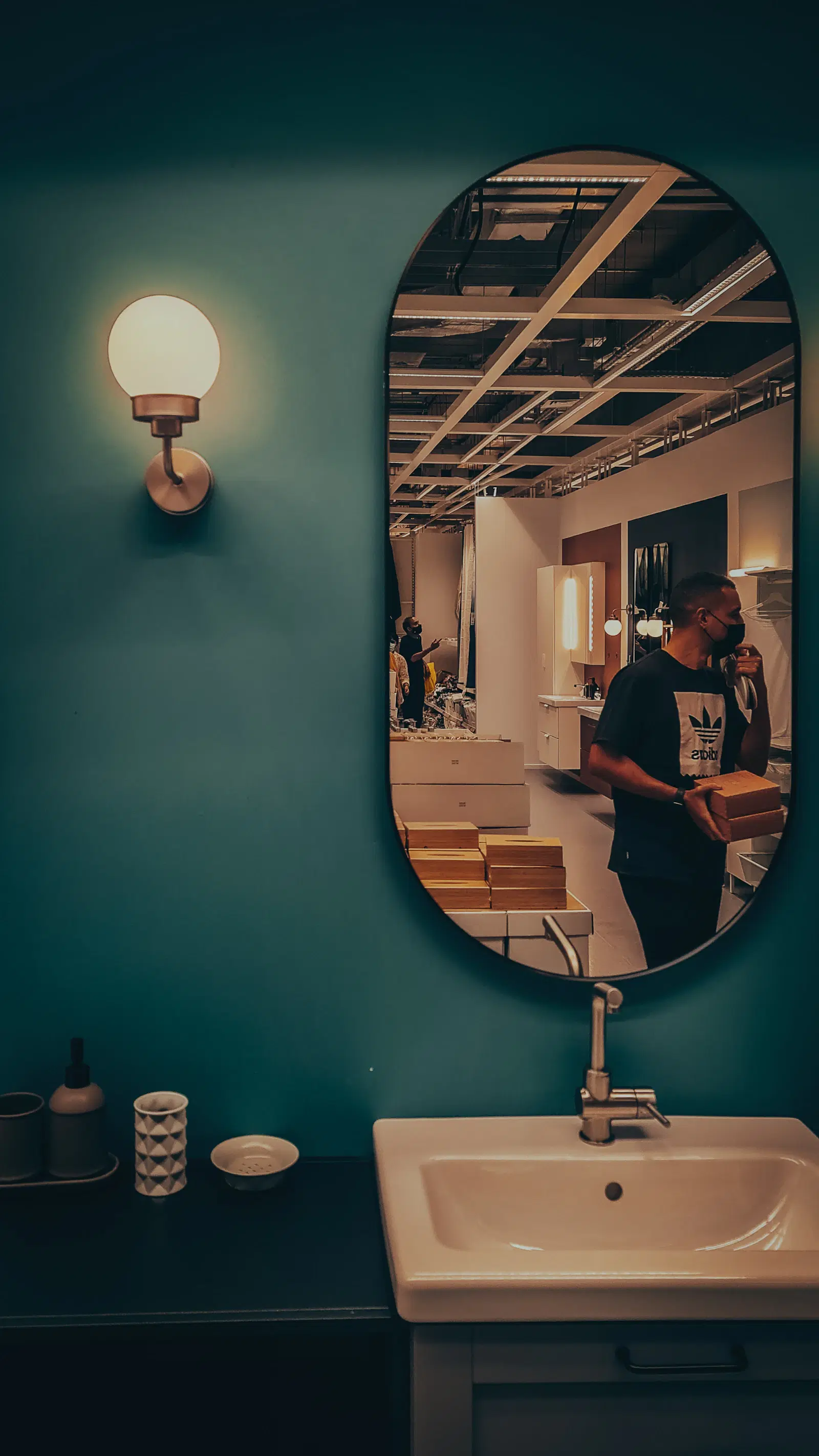 A man reflected in an oval bathroom mirror above a sink