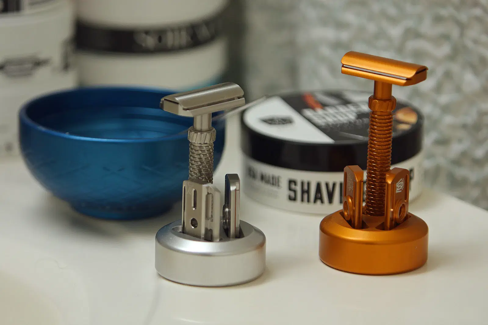 Two safety razors on stands beside a blue shaving bowl and a tub of shaving soap