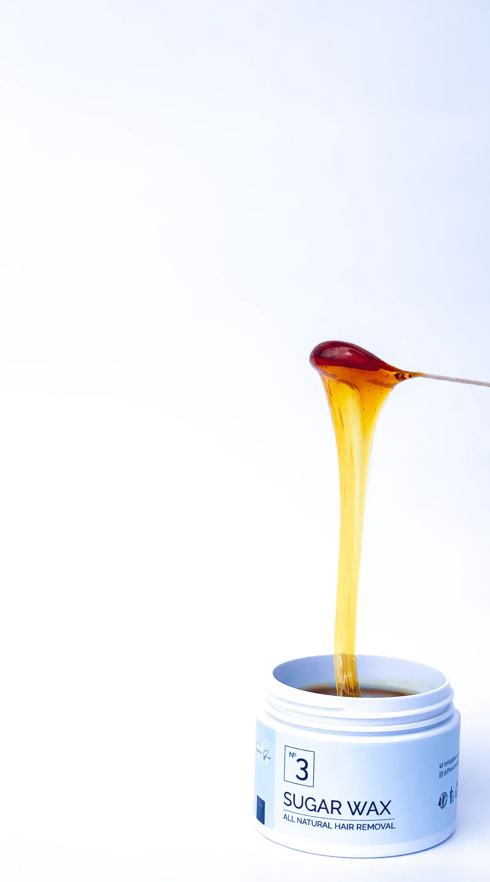 Sugar wax dripping from a wooden stick into an open jar labeled sugar wax