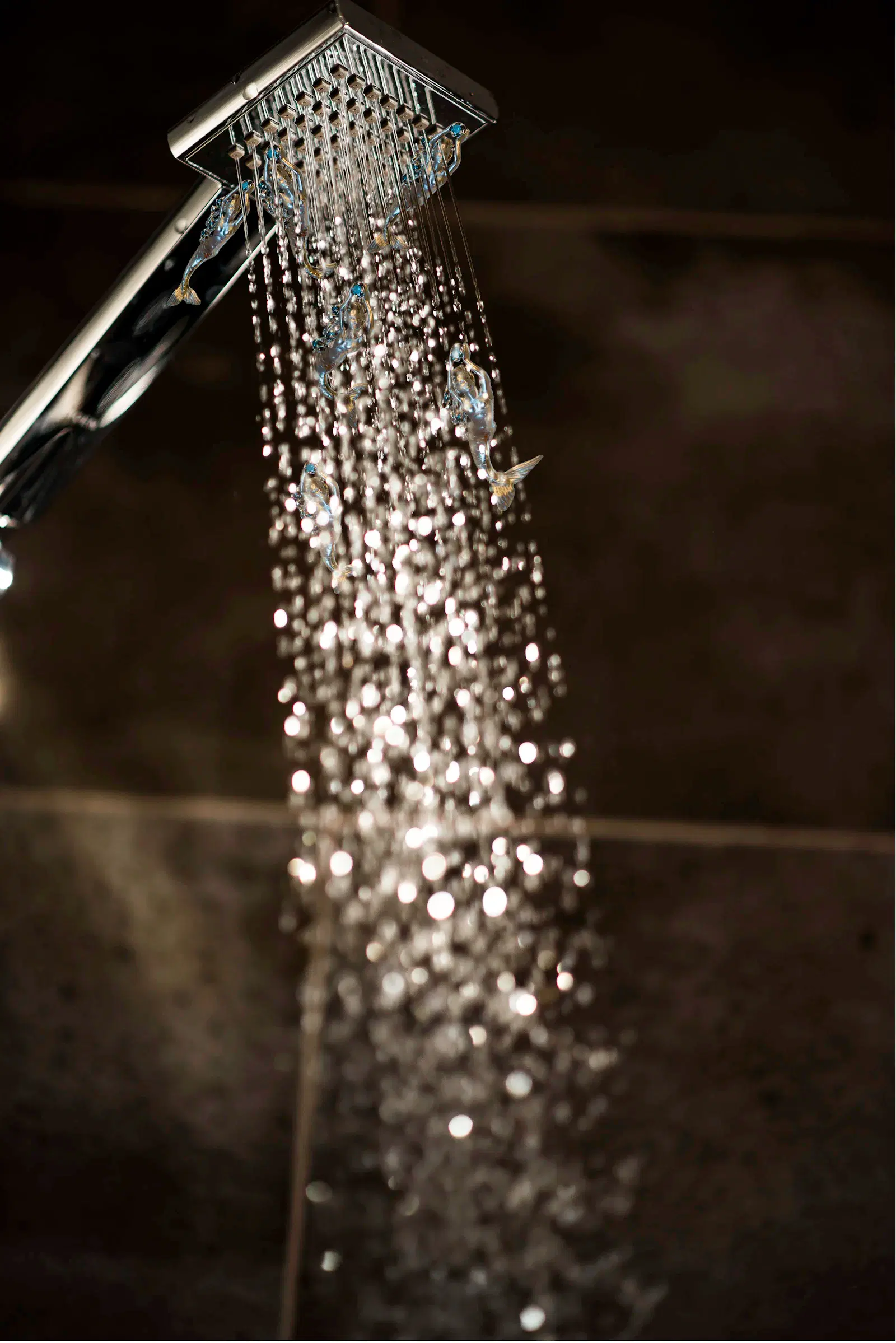 Water spraying from a shower head against a dark tiled wall