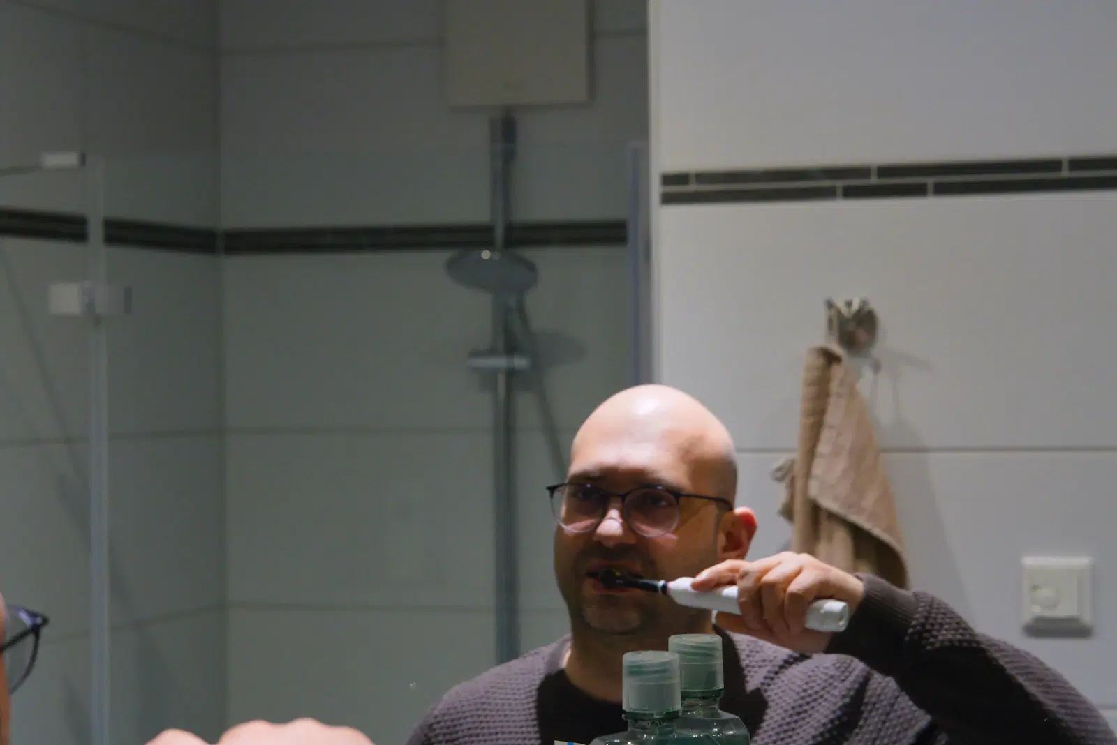 A man in glasses brushing his teeth in front of a bathroom mirror