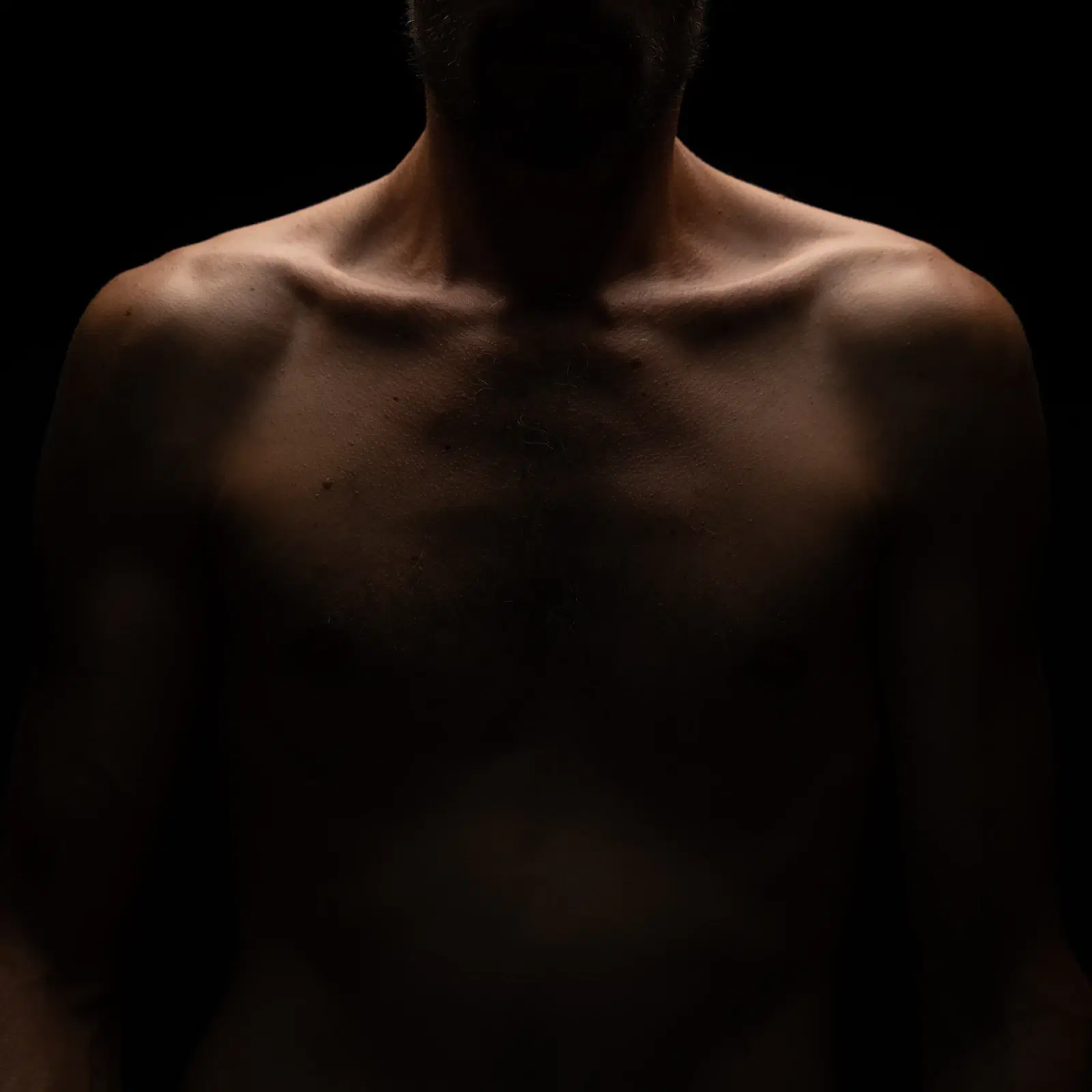 A man's bare chest and shoulders in low light