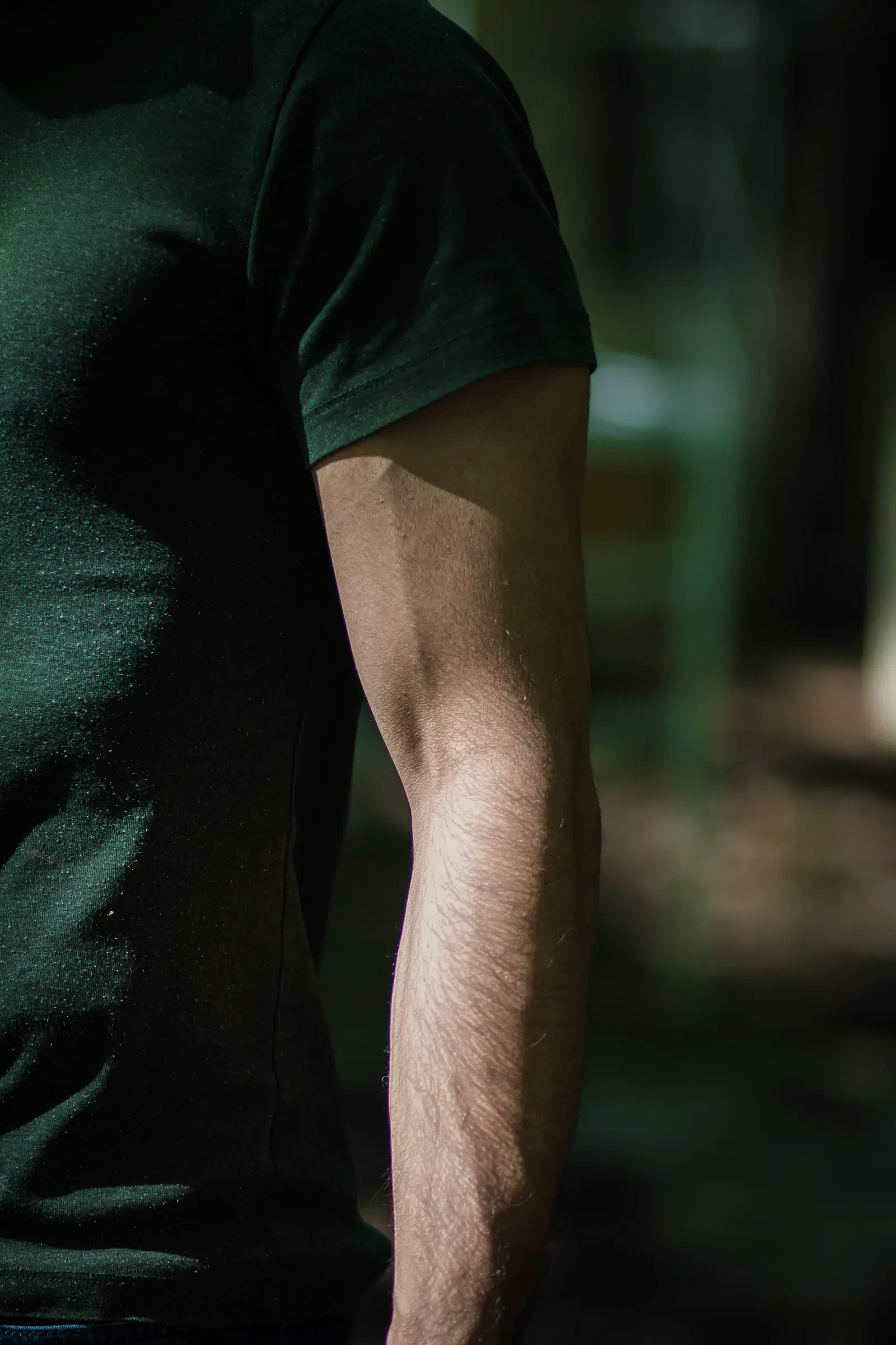 Sunlit hair on the forearm of a man in a dark green T-shirt