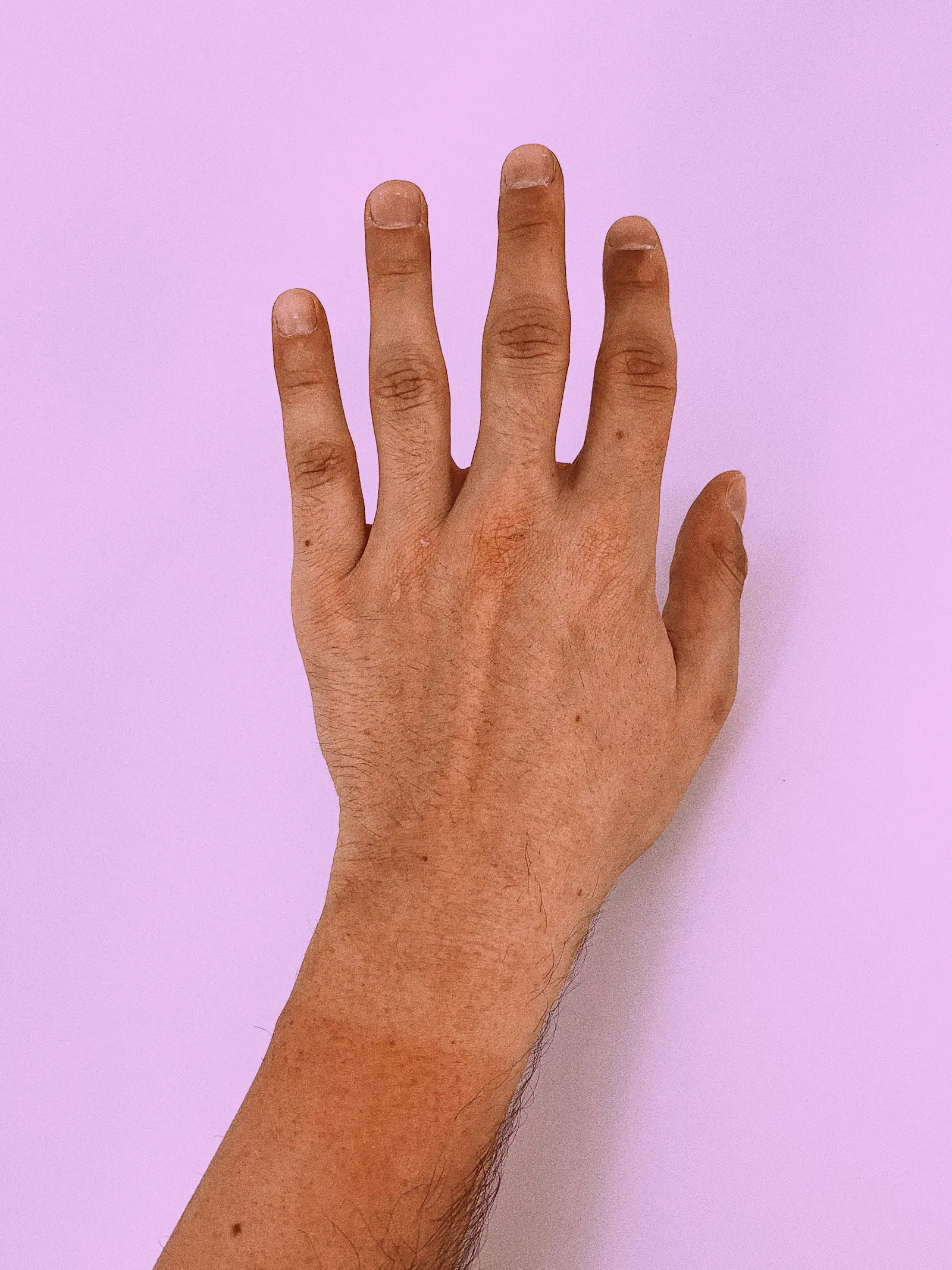 A hand and hairy forearm against a lilac background