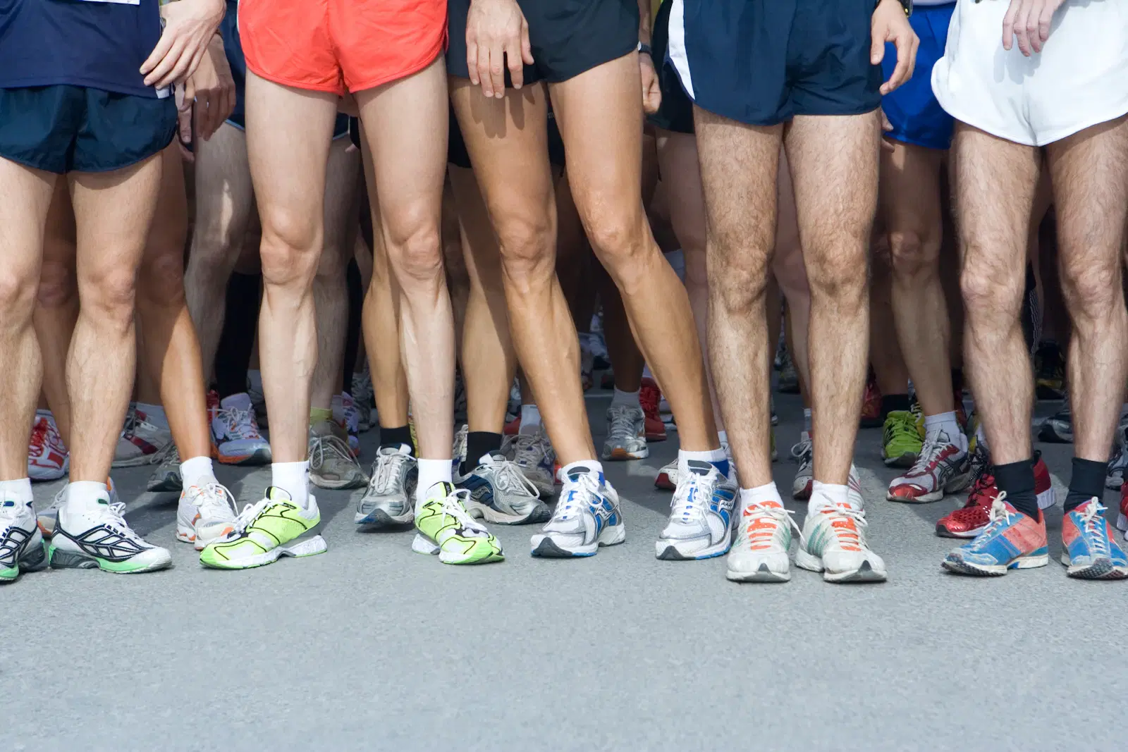 A row of runners' legs in shorts and sneakers at a race start line