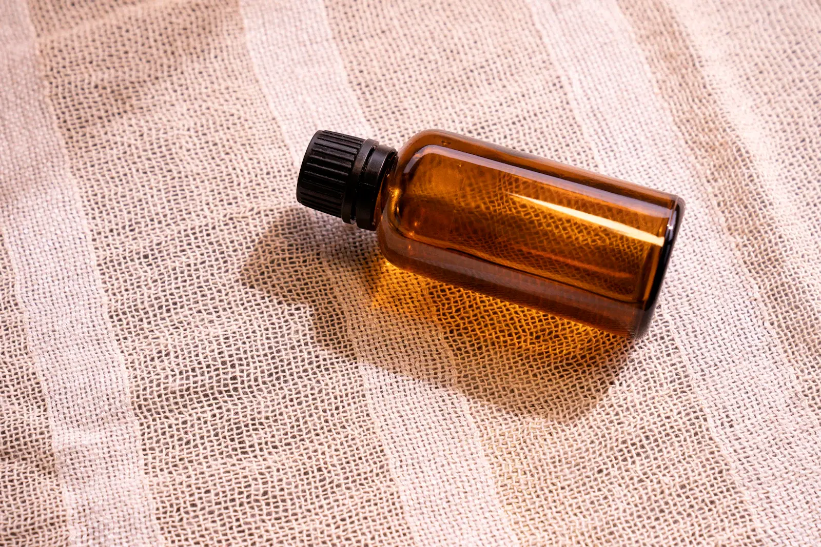 An amber glass bottle of body oil on a striped linen cloth