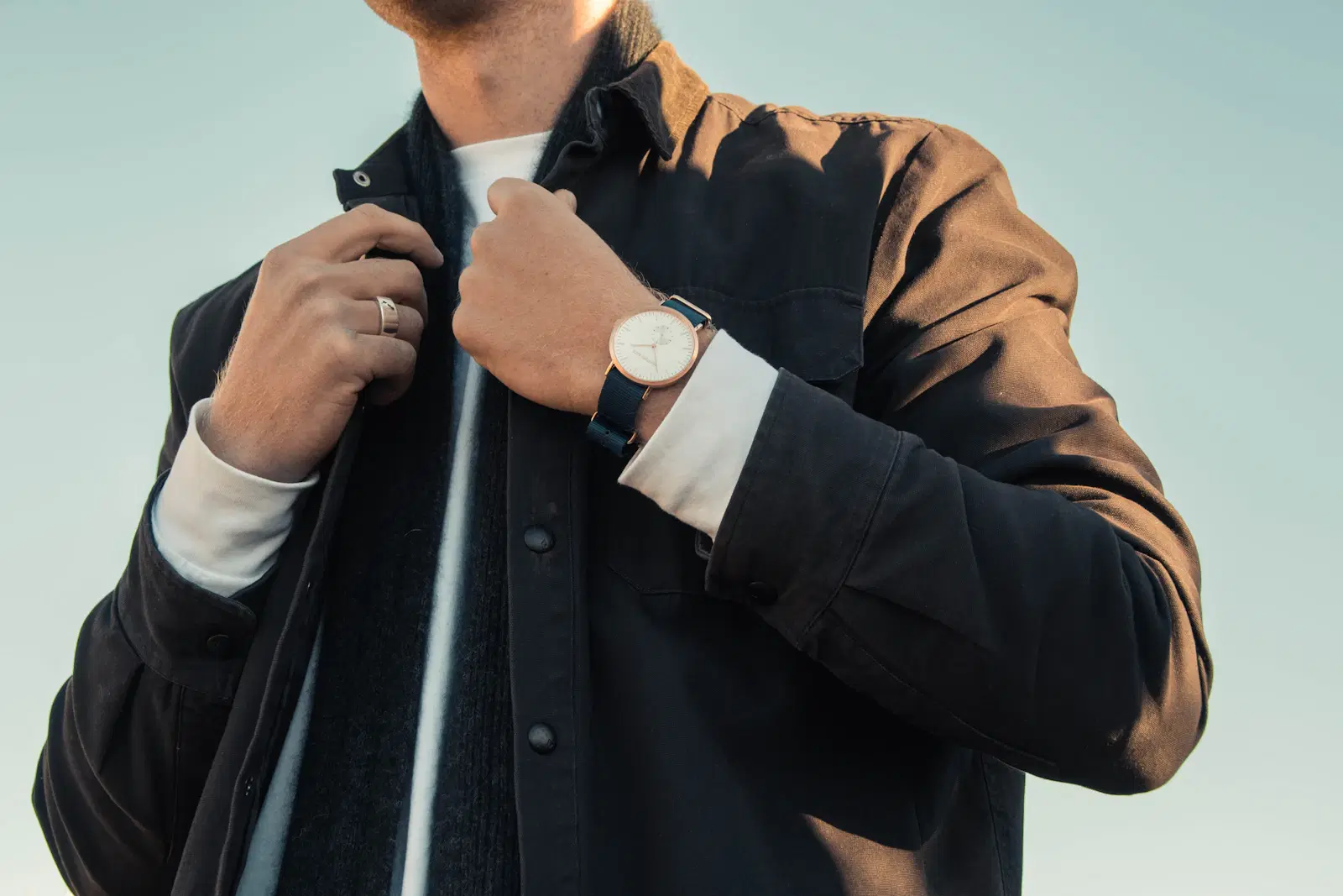 A man in a dark overshirt and wristwatch adjusting his collar
