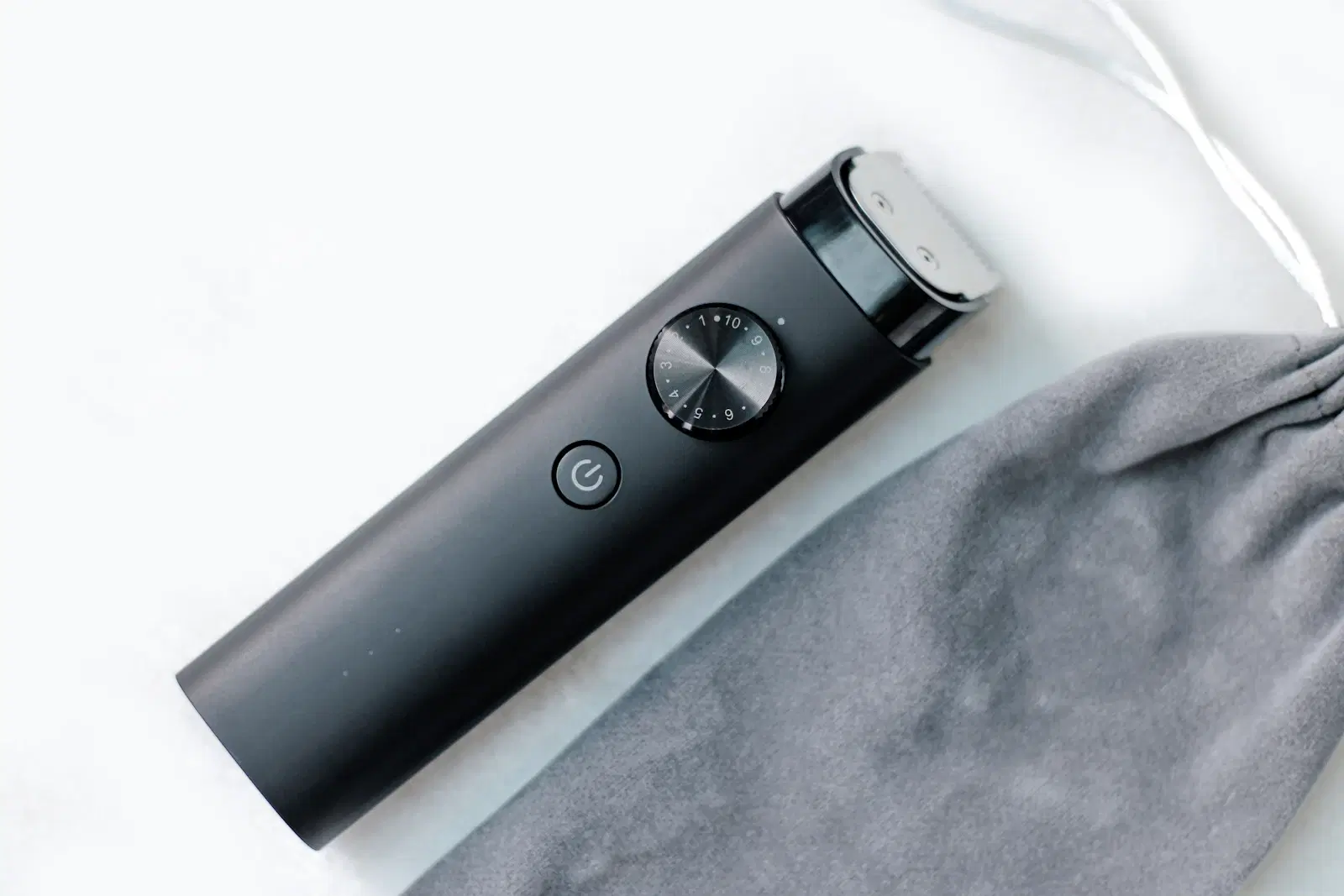 A black electric trimmer with a length dial lying next to a gray pouch