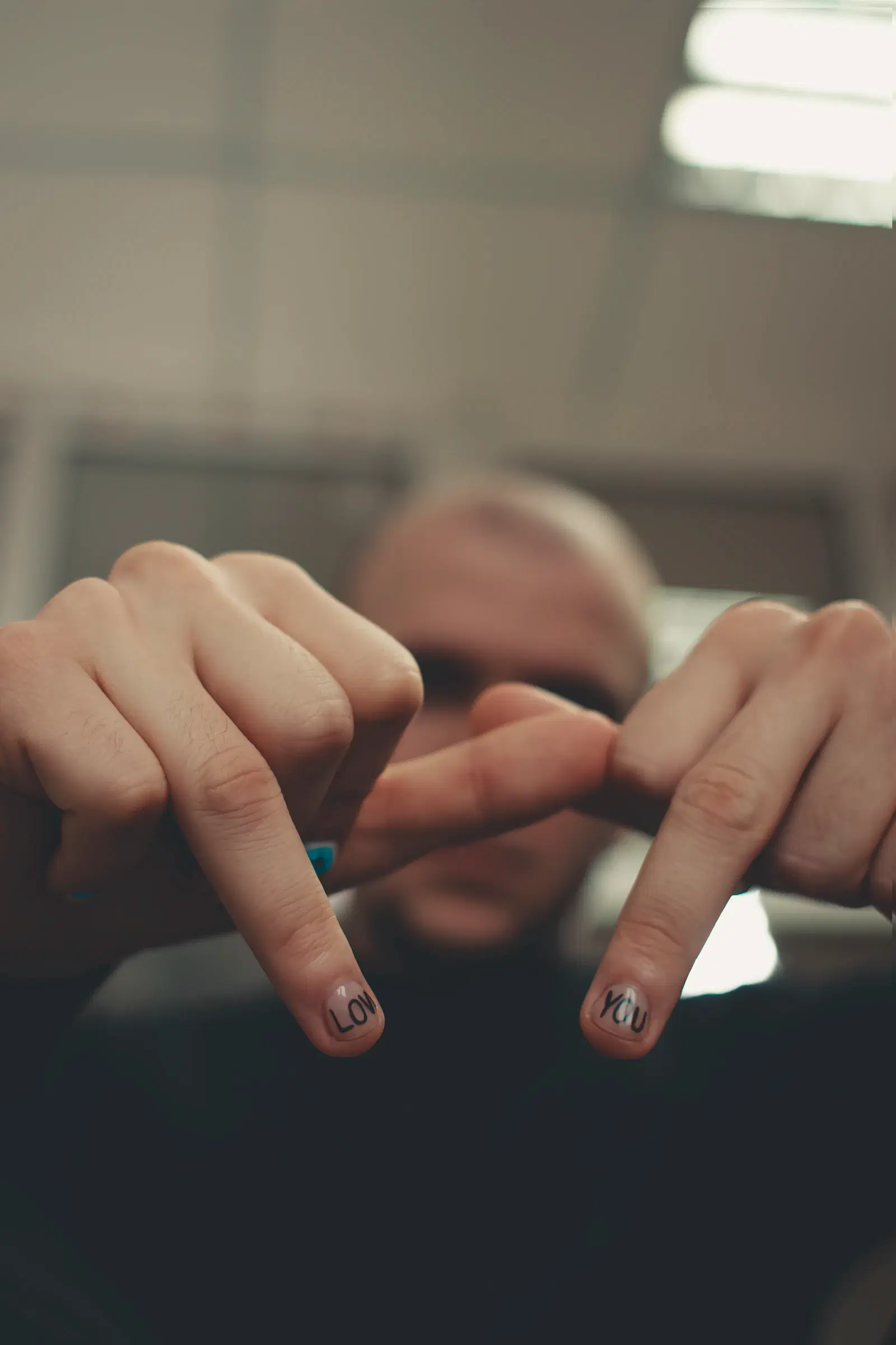 A man holding his hands up to the camera, with LOVE and YOU painted on two fingernails
