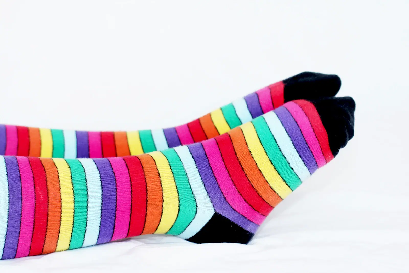 Rainbow striped thigh-high socks on a white bed