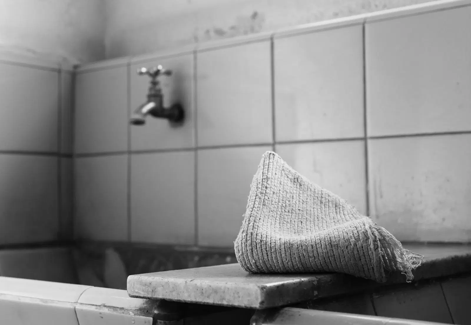 A knit washcloth draped on the edge of a tiled bathtub