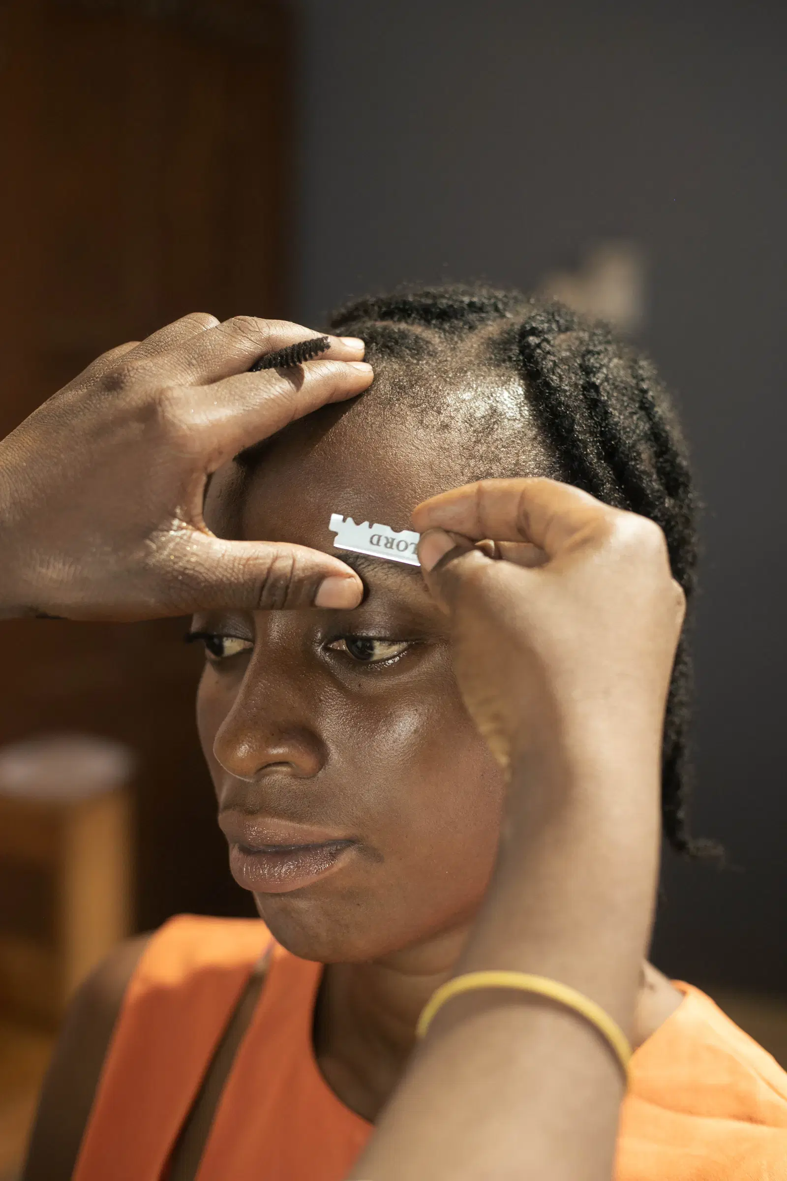 A brow artist cleaning up a client's brow line with a small razor blade and a spoolie brush