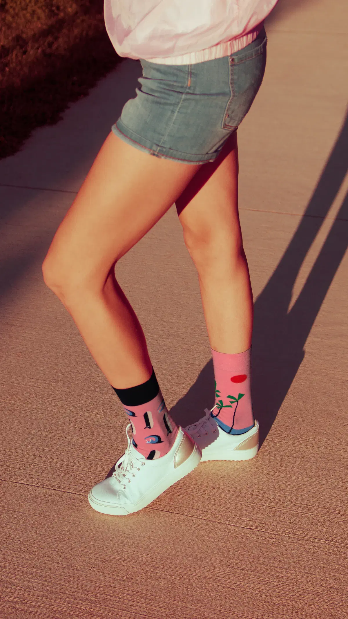 Denim shorts with mismatched pink patterned crew socks and white sneakers