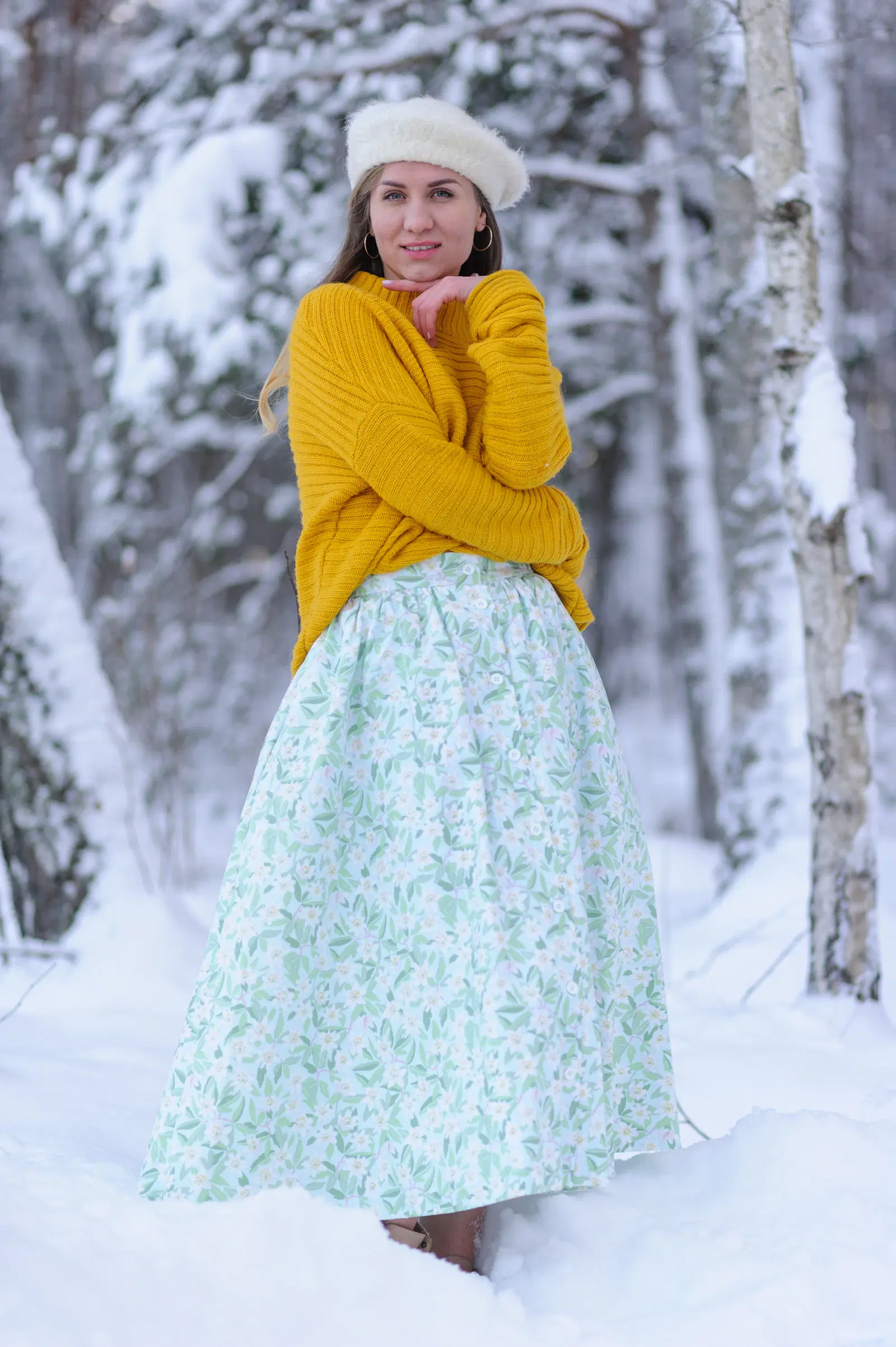 Yellow knit sweater with a long mint floral skirt and a white beret in a snowy forest