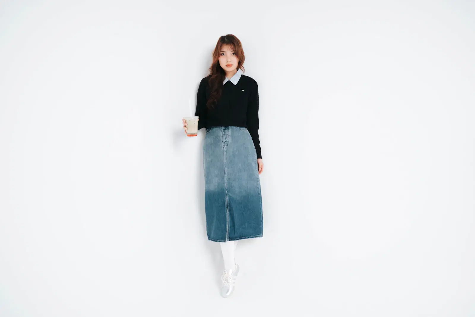 Long denim skirt with a front slit, worn with a black cable-knit sweater, white tights, and silver sneakers
