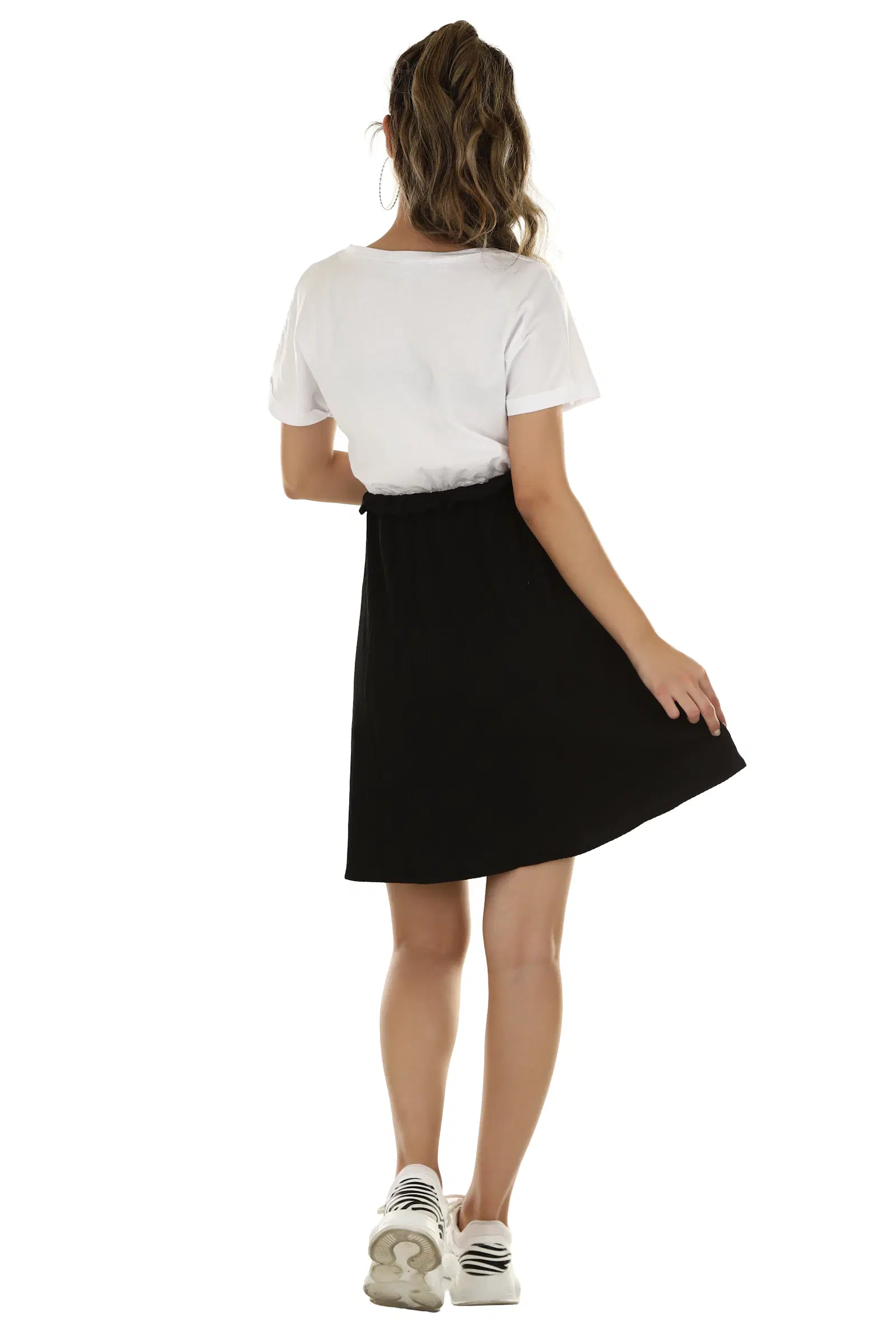 Black flared skirt worn with a white tee and white sneakers, seen from behind