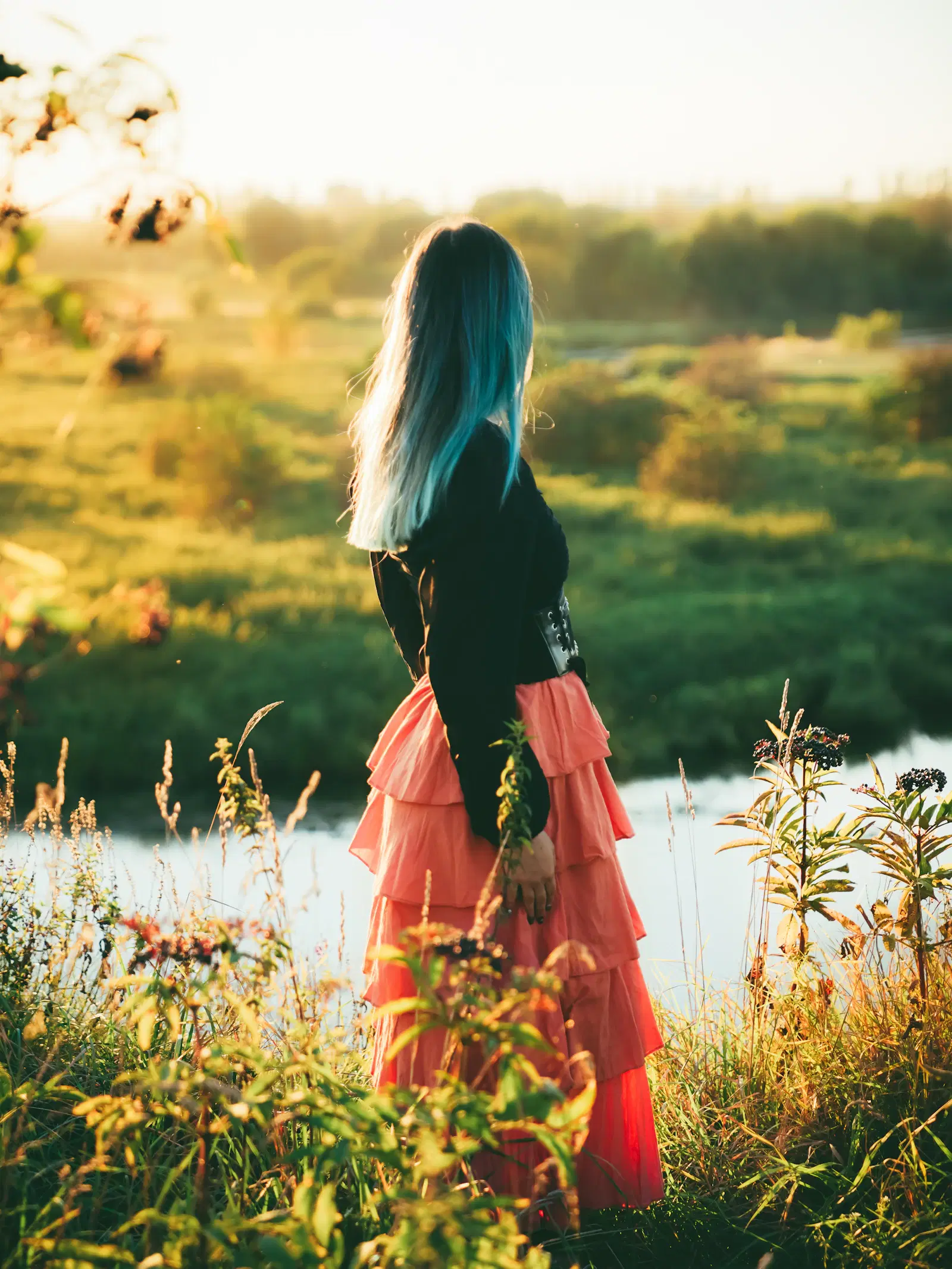 Coral tiered ruffle skirt worn with a black long-sleeve top and lace-up belt, by a river