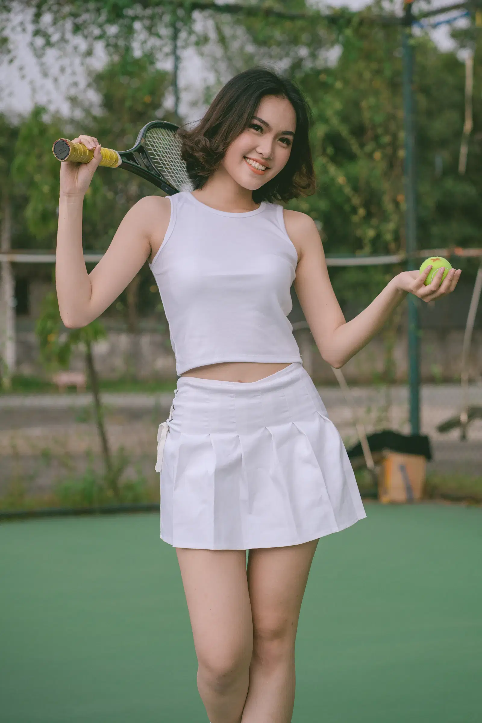 White pleated tennis skirt with a white tank top on a tennis court