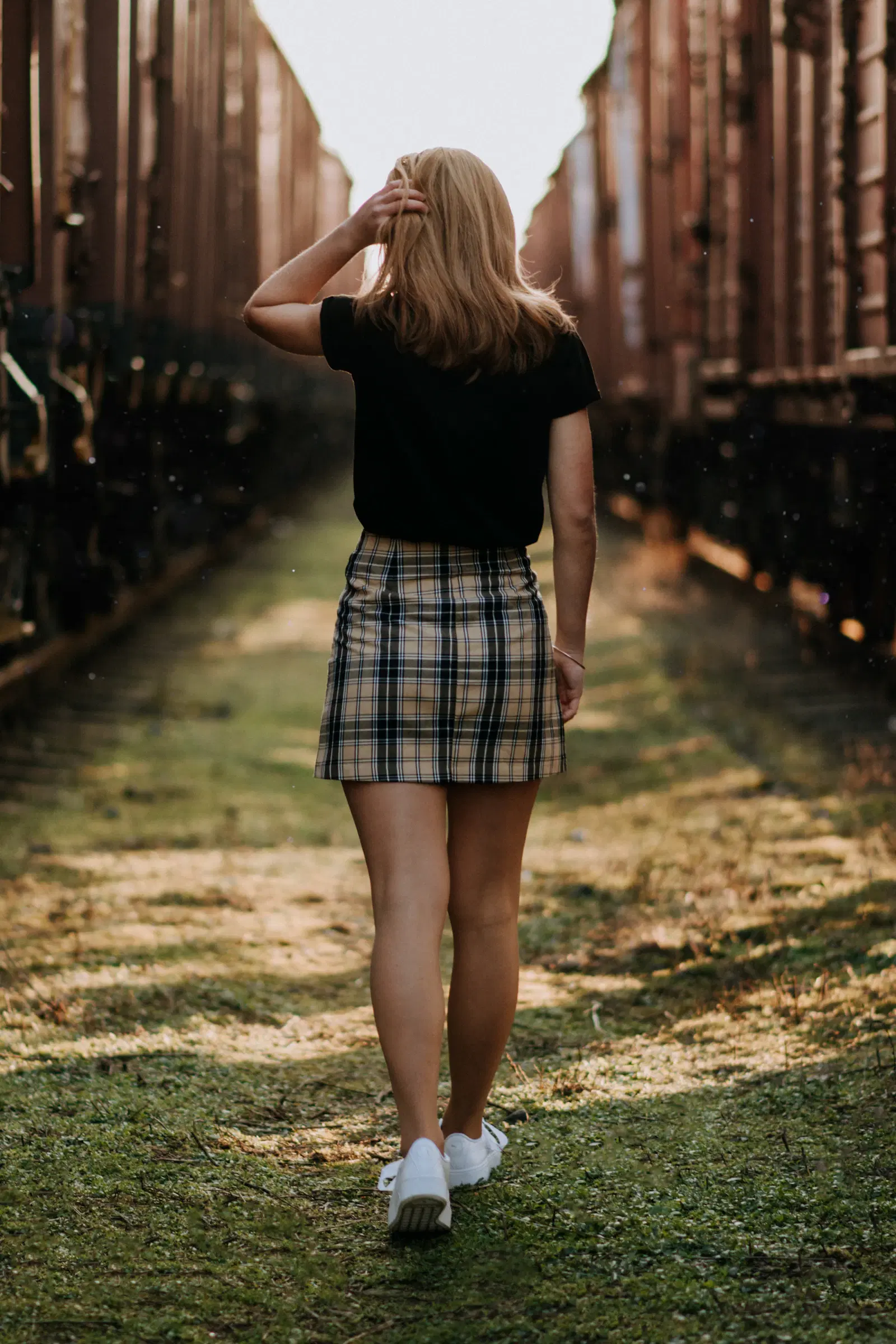 Tan and black plaid mini skirt hitting mid-thigh, worn with a black tee and white sneakers, seen from behind