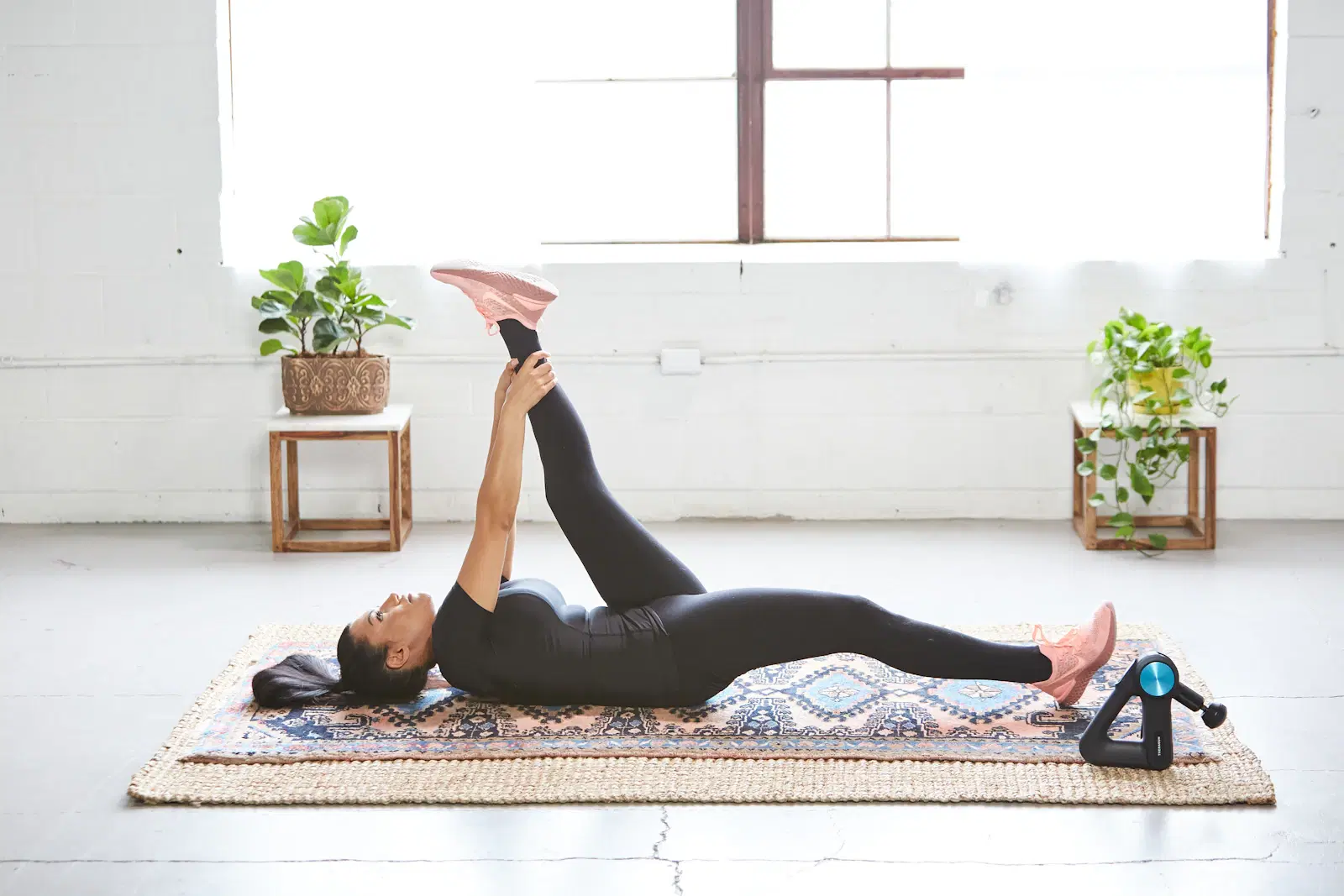 Person lying on their back on a patterned rug with one straight leg raised, the same flat-back floor position used for dead bugs
