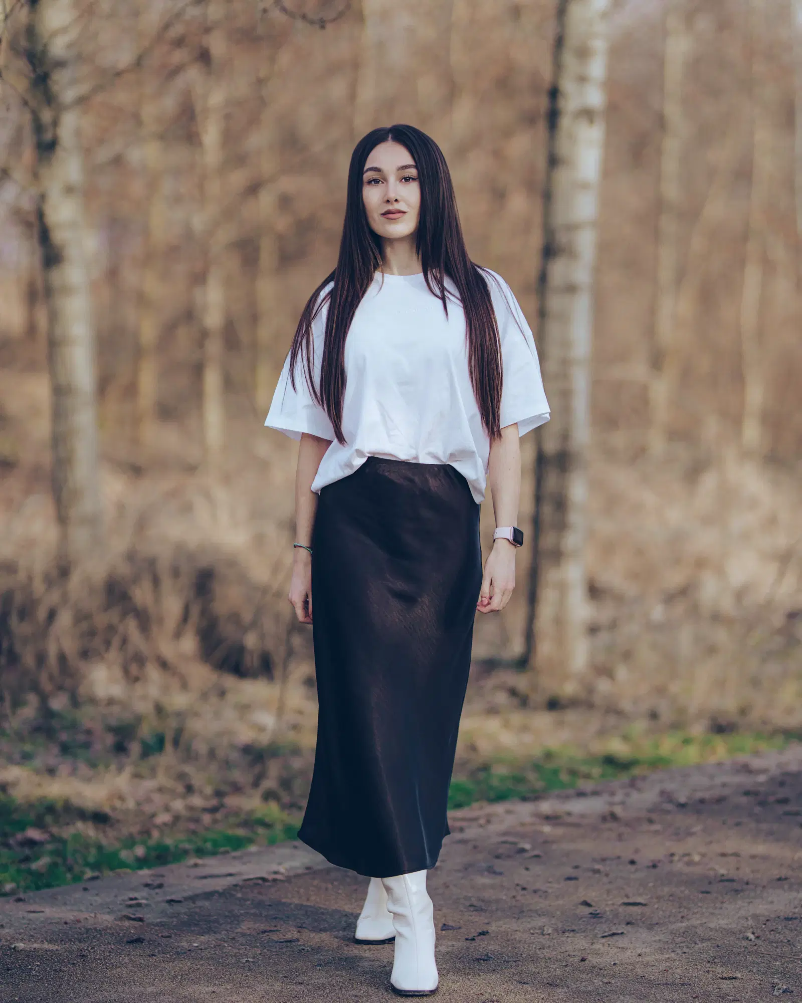 Dark satin midi skirt with a loosely tucked oversized white tee and white boots, an outfit that marks the waistline