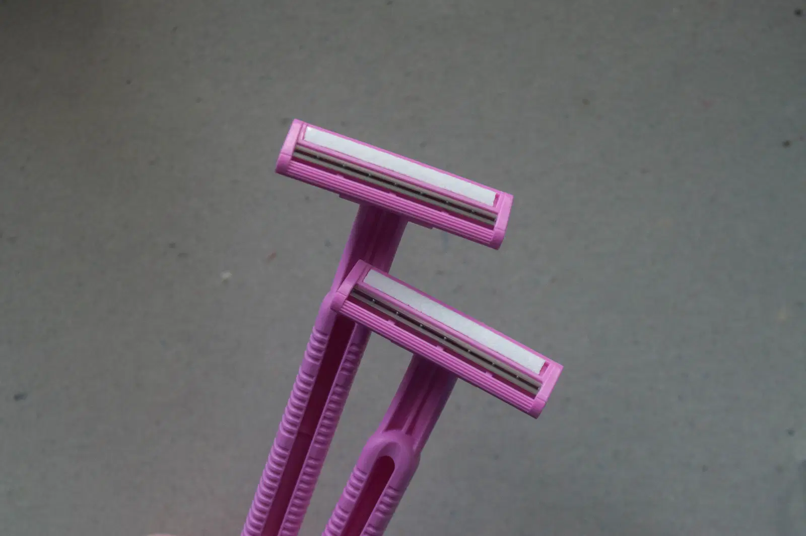 Two pink disposable razors on a gray background