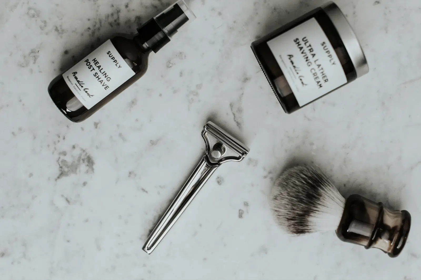 Razor, shaving brush, shaving cream, and post-shave spray laid out on a marble counter