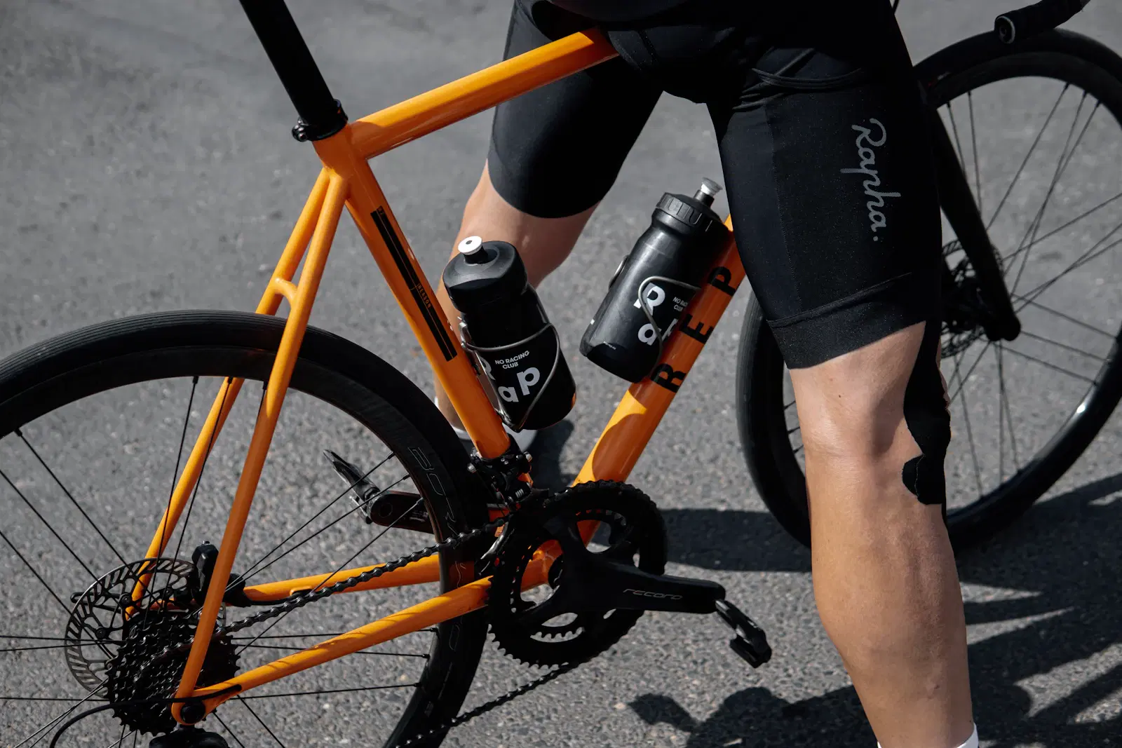 A cyclist in black bike shorts standing over an orange bike