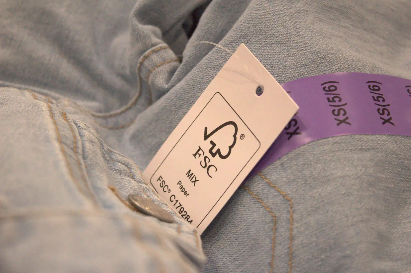 A paper hang tag and a size sticker on a pair of light-wash jeans