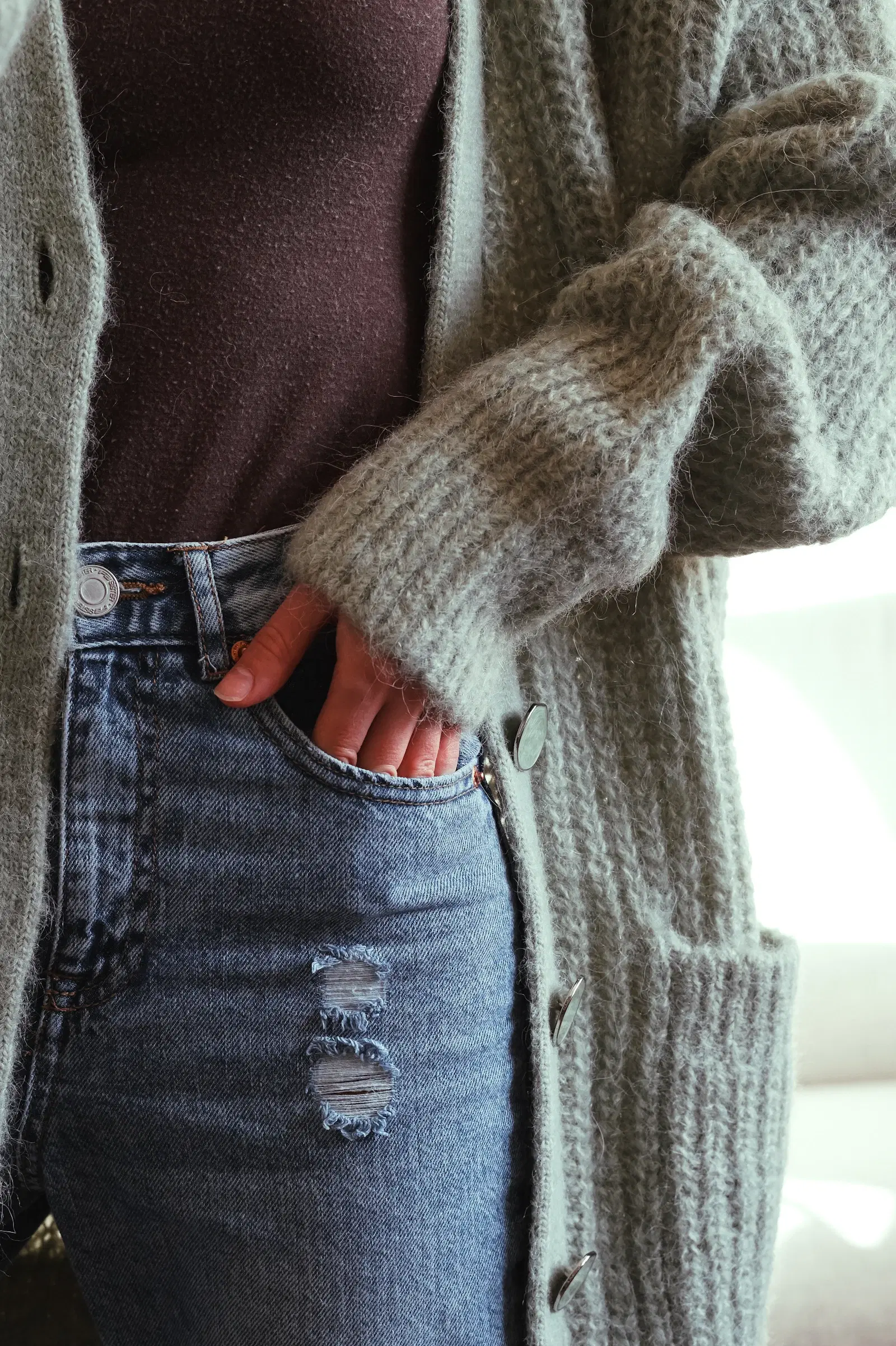 A gray knit cardigan worn open over a dark top and high-waisted jeans