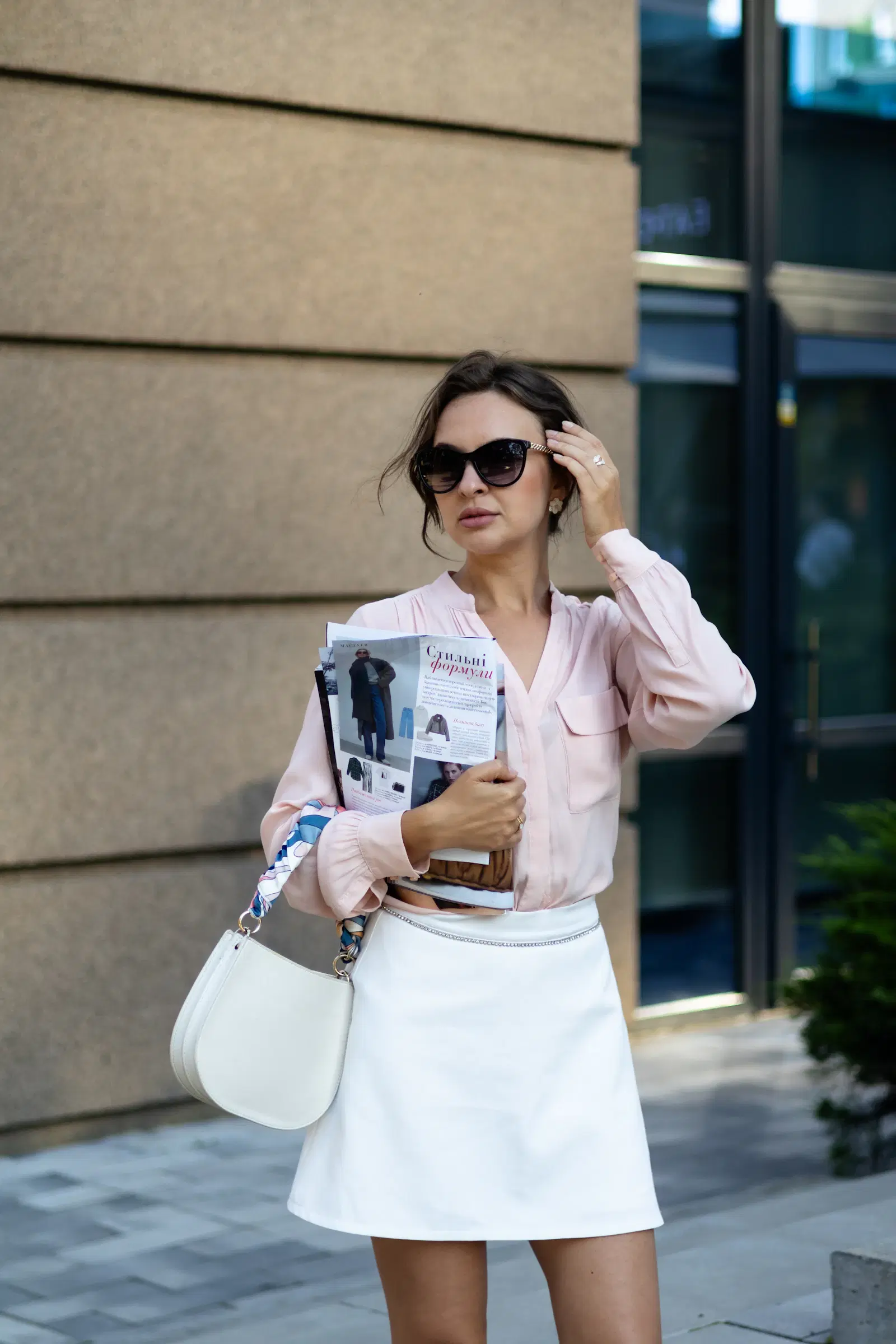 A pastel pink blouse with a white A-line skirt and white shoulder bag