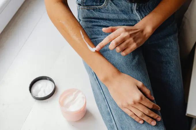 A person applying hand cream to their forearm, demonstrating post-shave hydration