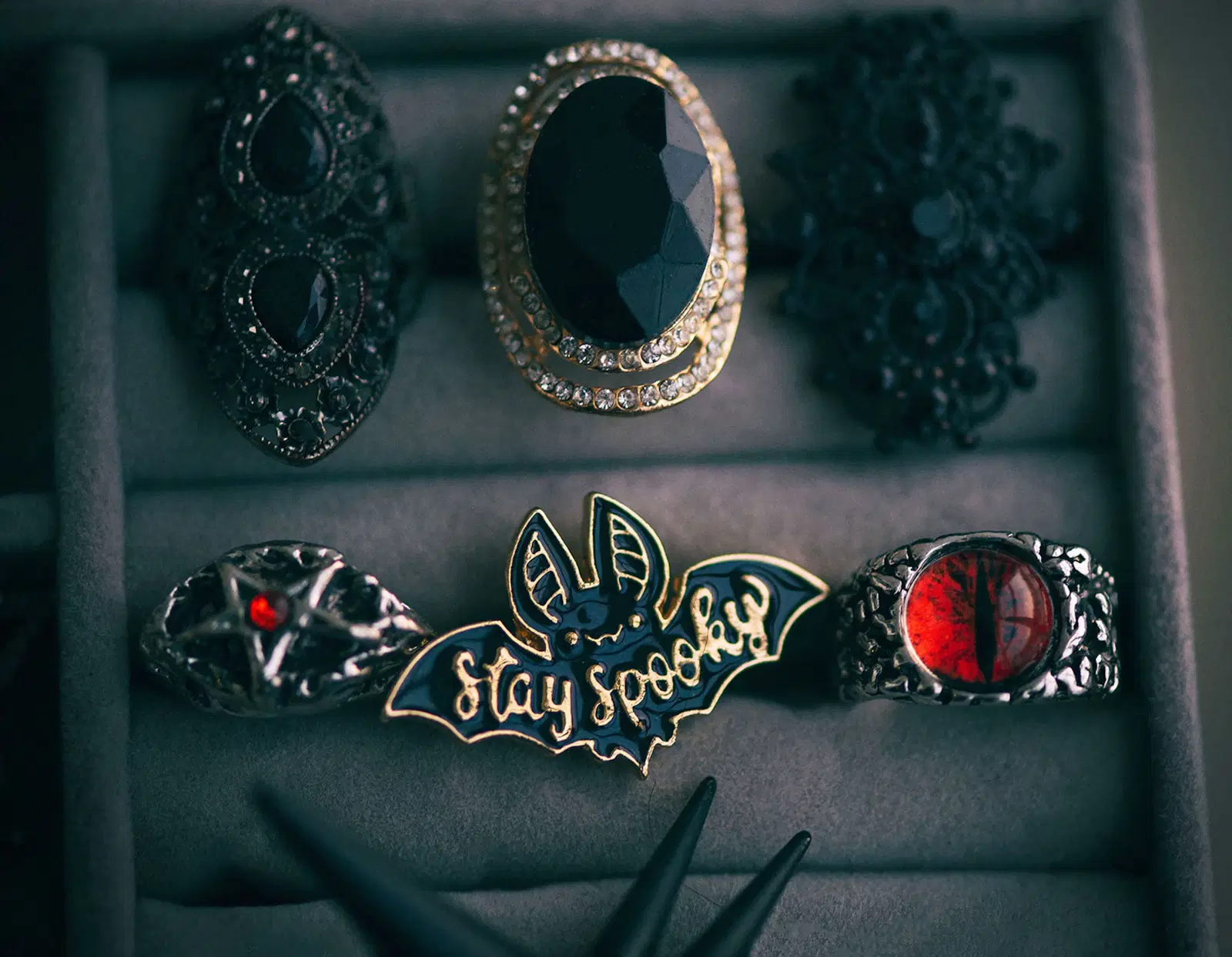 Gothic statement rings and a bat-shaped enamel pin in a jewelry tray