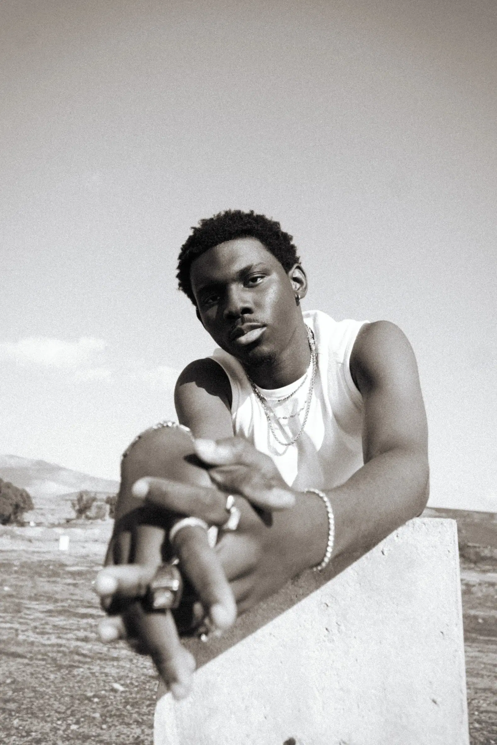 A man in a white tank top wearing several rings, a bracelet, and a chain necklace