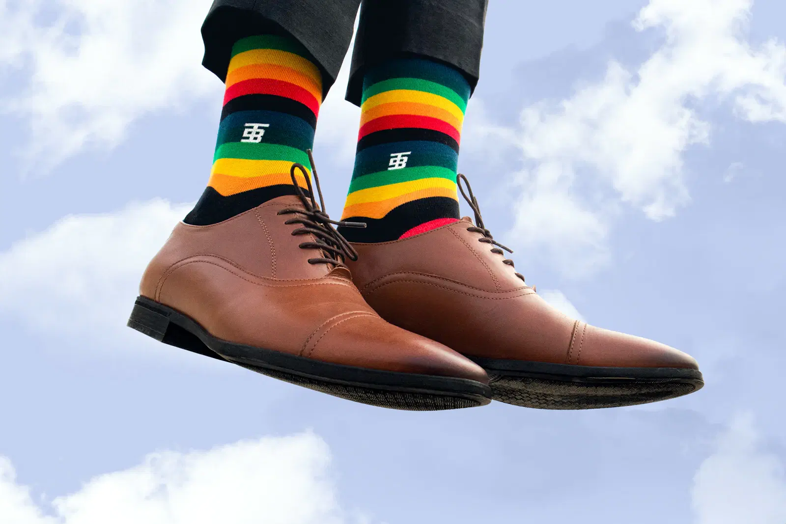 Rainbow striped socks with brown leather shoes against a blue sky