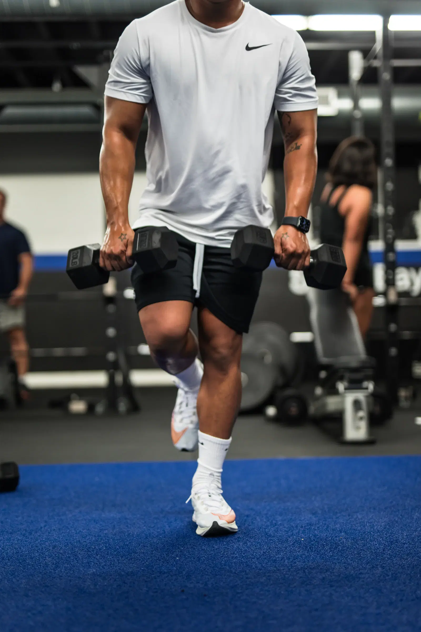 Man mid-stride in a walking lunge with a dumbbell in each hand, the same loaded grip used for split squats