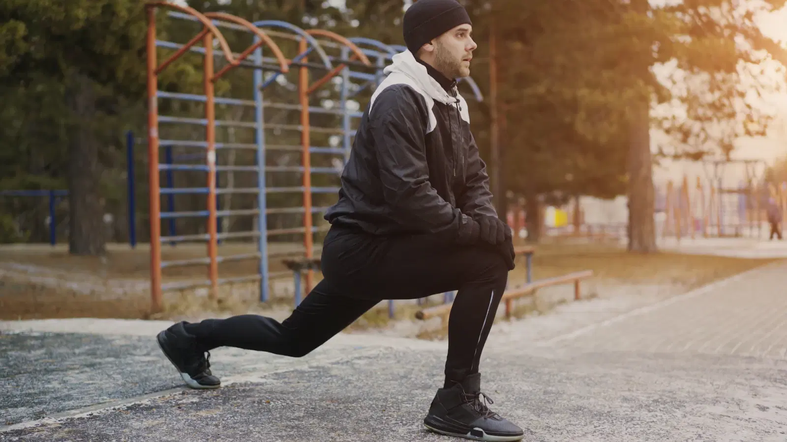 Man in winter workout clothes holding a deep forward lunge outdoors, working the thigh muscles
