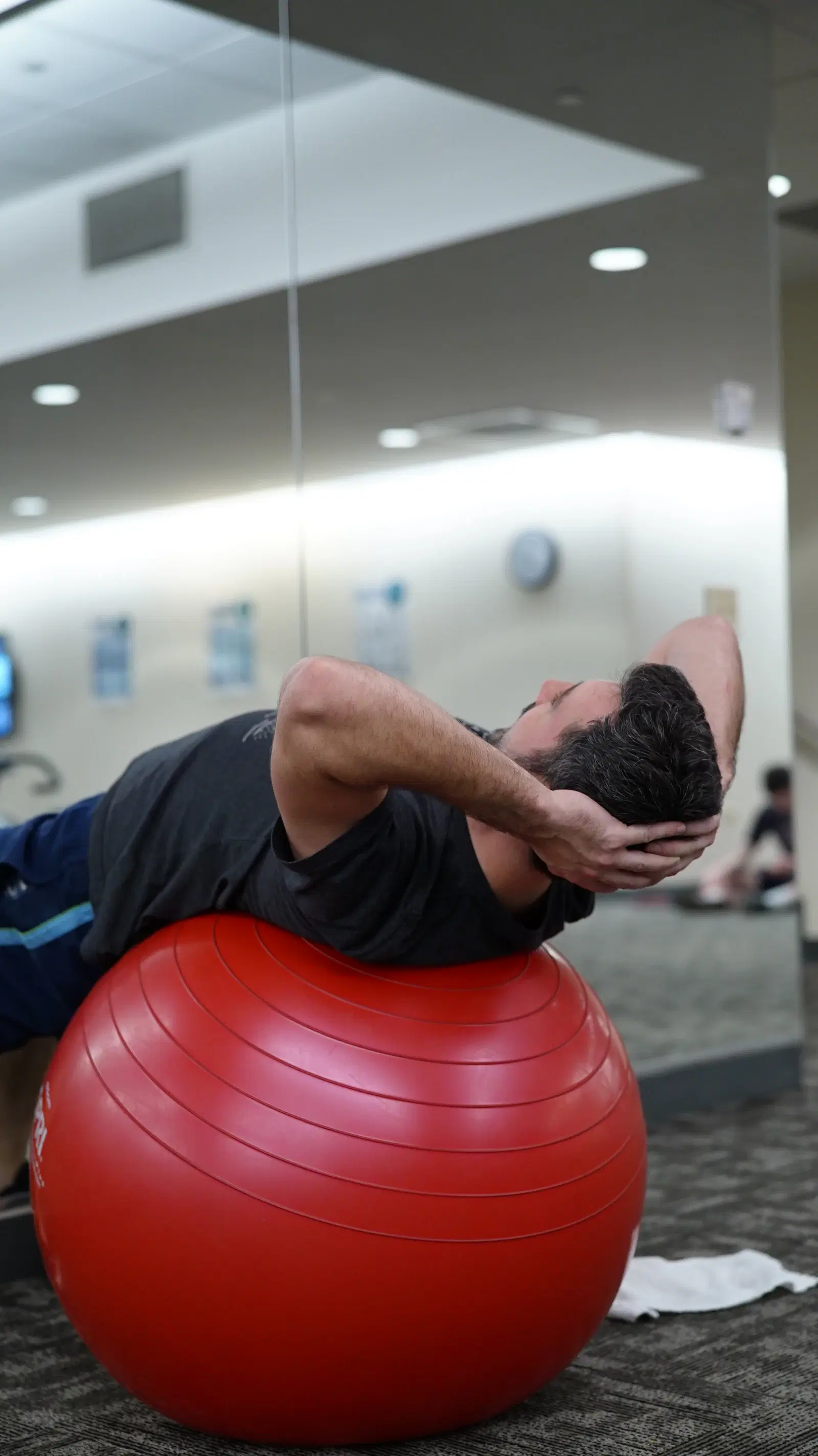 Man doing a crunch on a large red stability ball in a gym