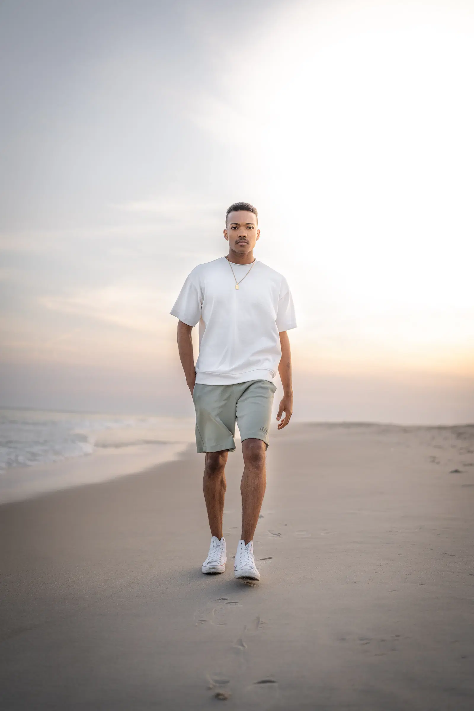 Man walking on a beach in a white tee and above-the-knee shorts, the kind of outfit where thigh chafing starts