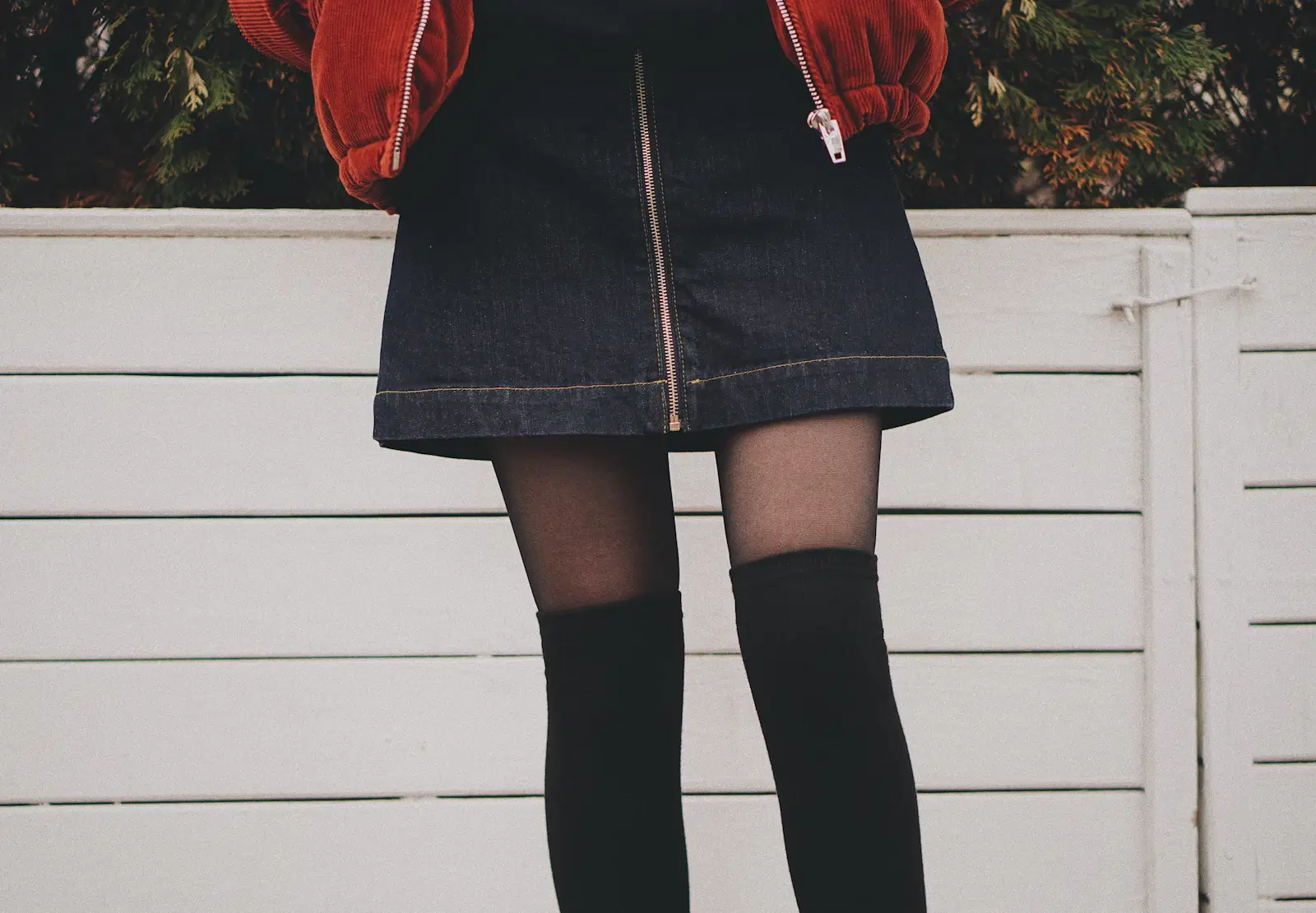 Black over-the-knee socks layered over sheer tights with a zip-front denim mini skirt and a rust corduroy jacket